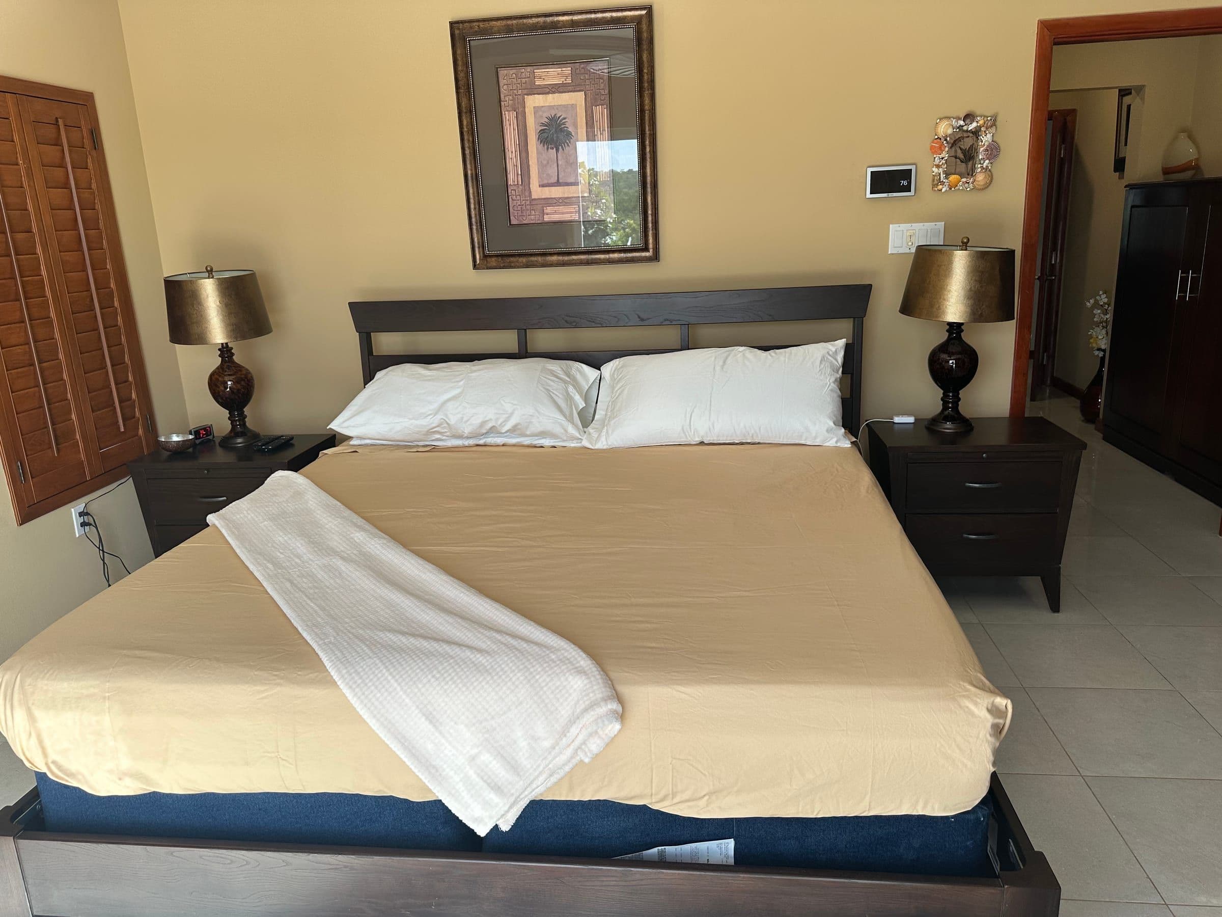 The primary bedroom. King bed, dark wood furniture, framed art, blackout shutters.