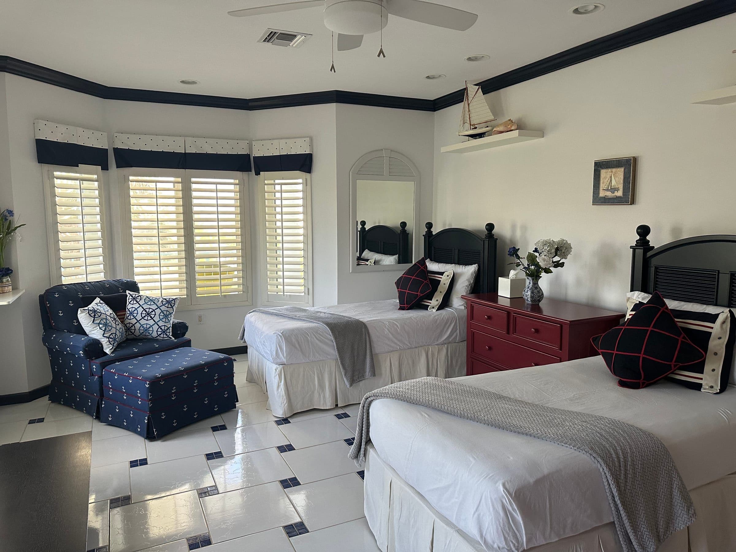 The twin bedroom. Two beds with navy nautical accents, white plantation shutters, ceiling fan.