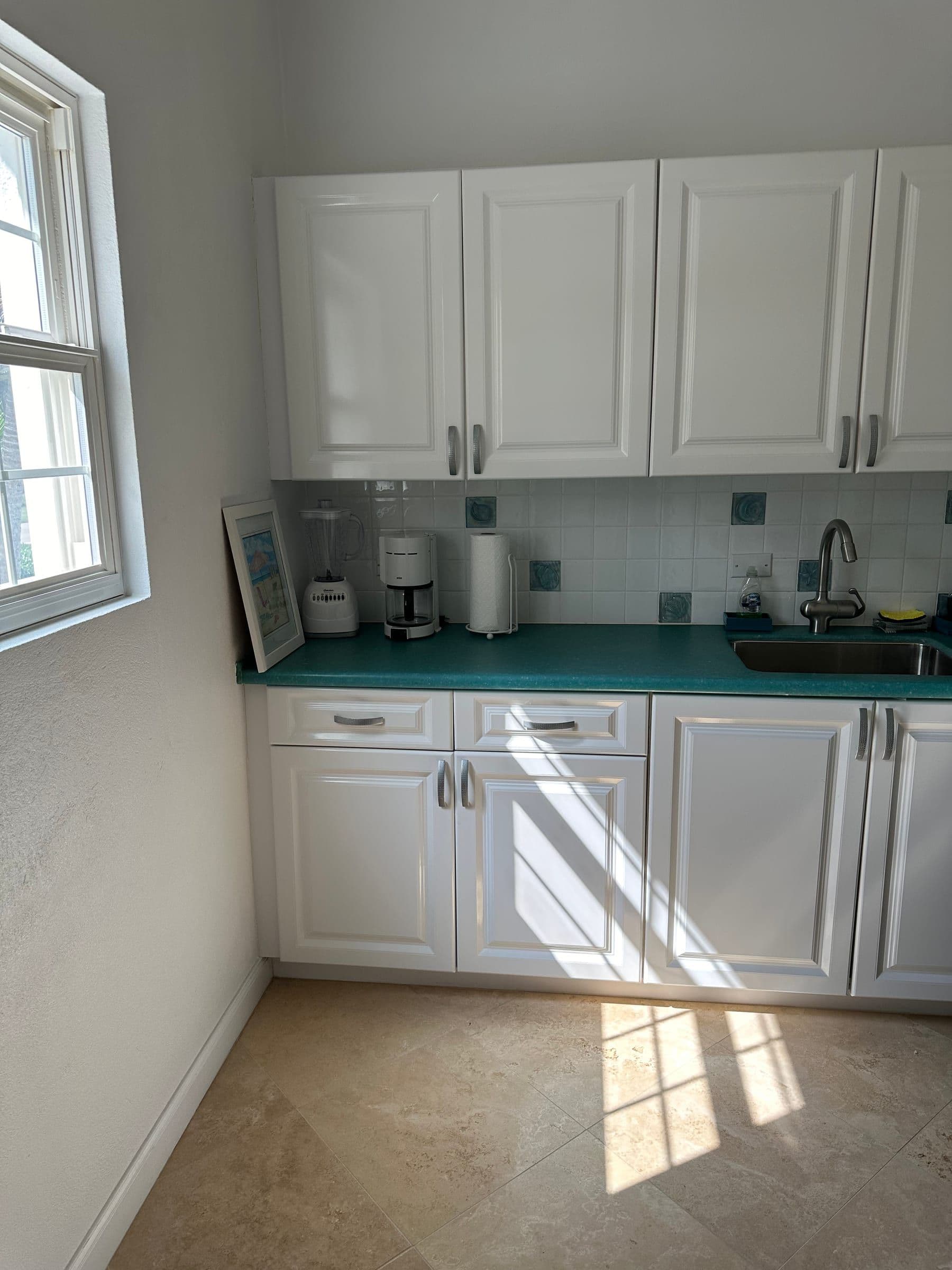 The cottage kitchen. Turquoise counter, white cabinets, coffee maker by the window.